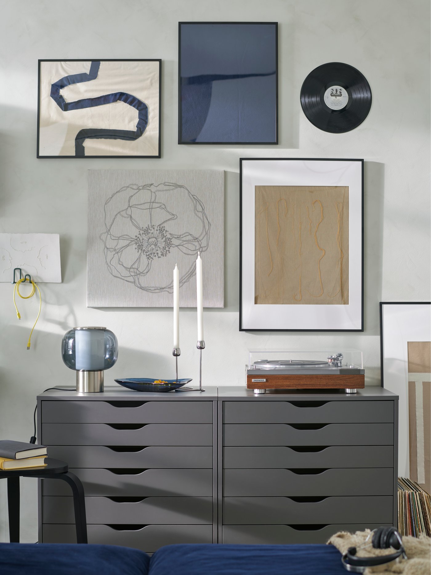 An art wall with LOMVIKEN frames and a vinyl record. A record player and HÖGVIND table lamp sit on two ALEX drawer units.