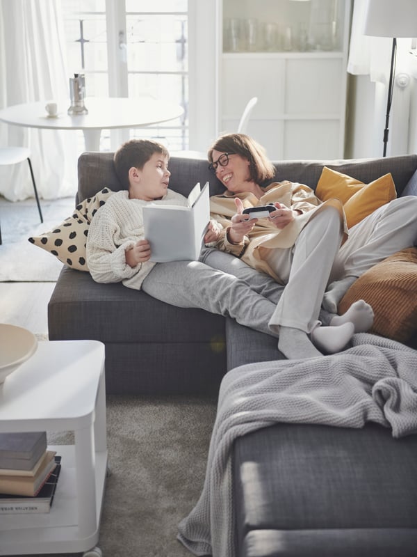 Woman and child lying in a FRIHETEN corner sofa, reading a story.