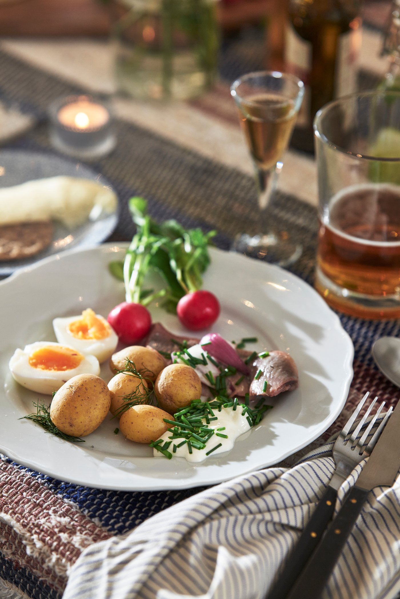 En utsökt tallrik med traditionell svensk midsommarmat, med färskpotatis, sill och ägg, serveras på ett vackert dukat bord.