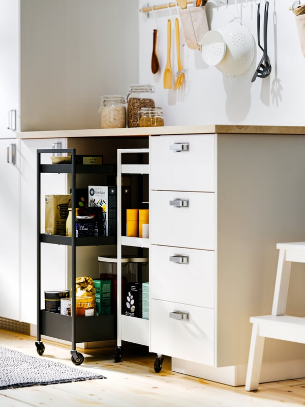 White METOD base cabinets with MAXIMERA interiors, an EKBACKEN worktop and two NISSAFORS trolleys, one black one white below.