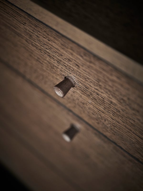 A close-up of the front of a brown oak-veneer TONSTAD dresser with 6 drawers showing two of the solid oak knobs.