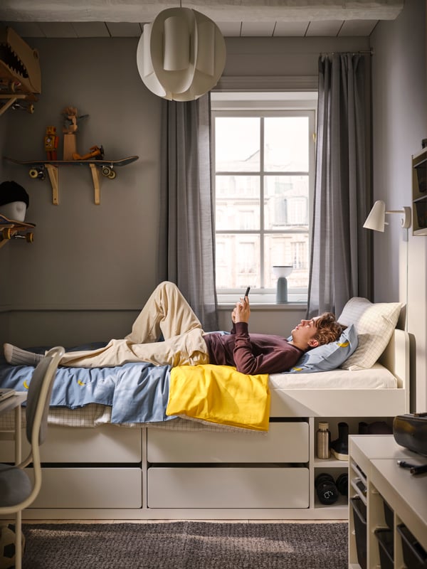 Cama con almacenage SLÄKT color blanco. Sobre ella un adolescente levendo.
