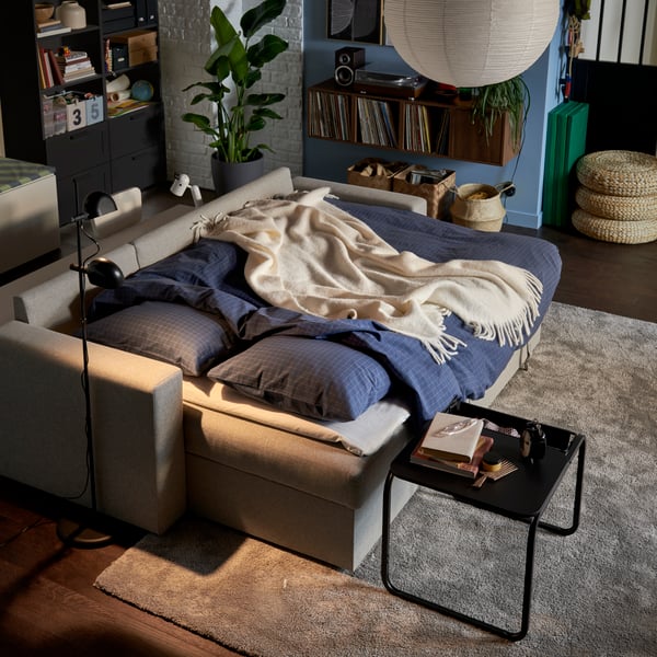 A dimly lit living room with a BÅRSLÖV sofa-bed made for the night with DOFTAKLEJA duvet cover and pillowcases.