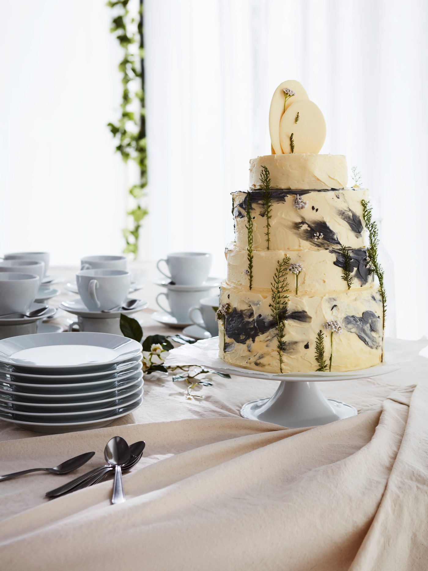 Un gran pastel sobre un soporte en una mesa de boda bien vestida con platos apilados detrás