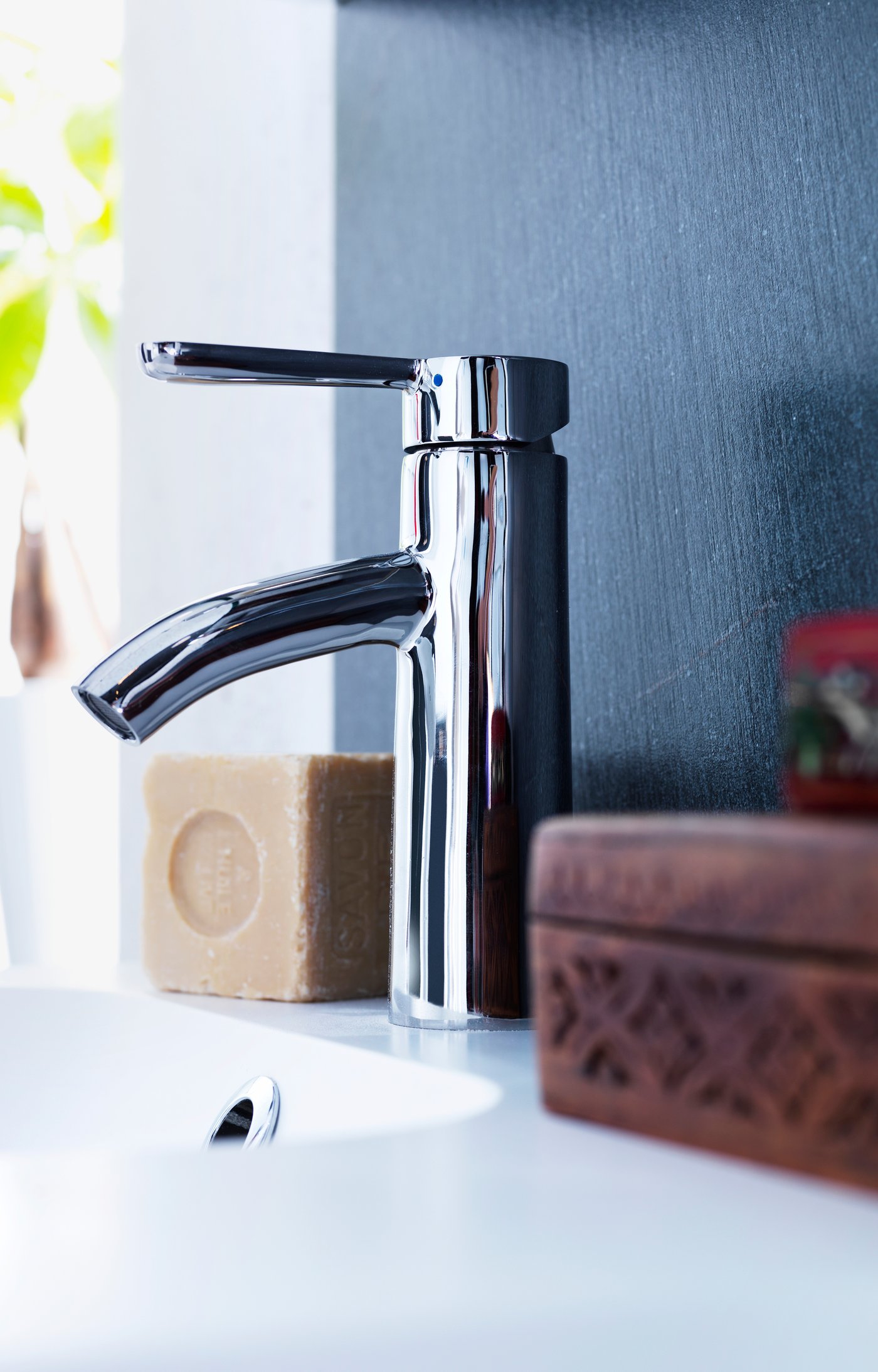 Mitigeur pour lavabo DALSKÄR en finition chromée à côté d’un savon, avec des accessoires de salle de bain à l’arrière-plan.