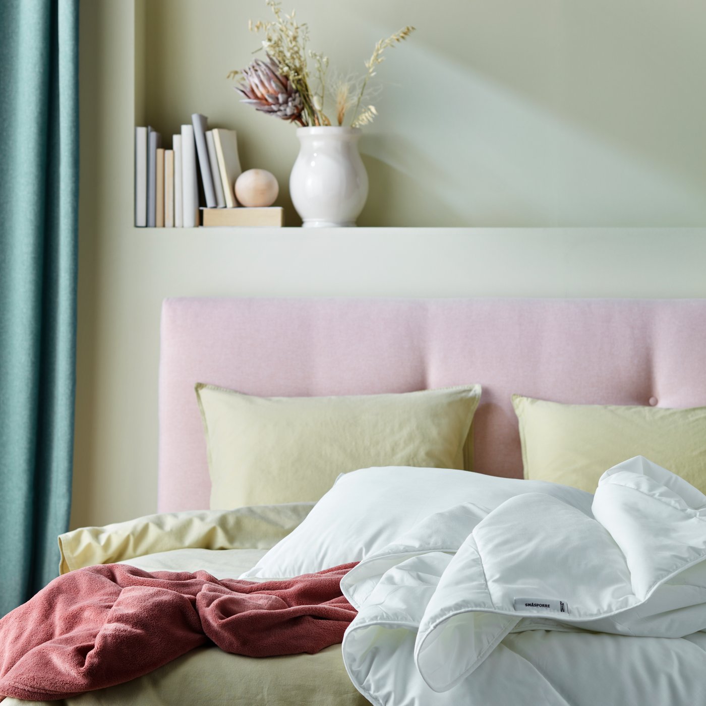 Close-up of a light pink upholstered bed with bedding in light yellow and dark pink. A white duvet and pillow on top.