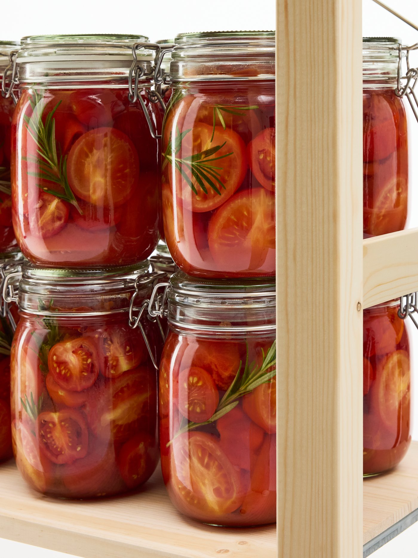 Close-up of an IVAR shelf unit in natural wood. On the shelf, a row of heavy glass jars that contain pickled tomatoes.