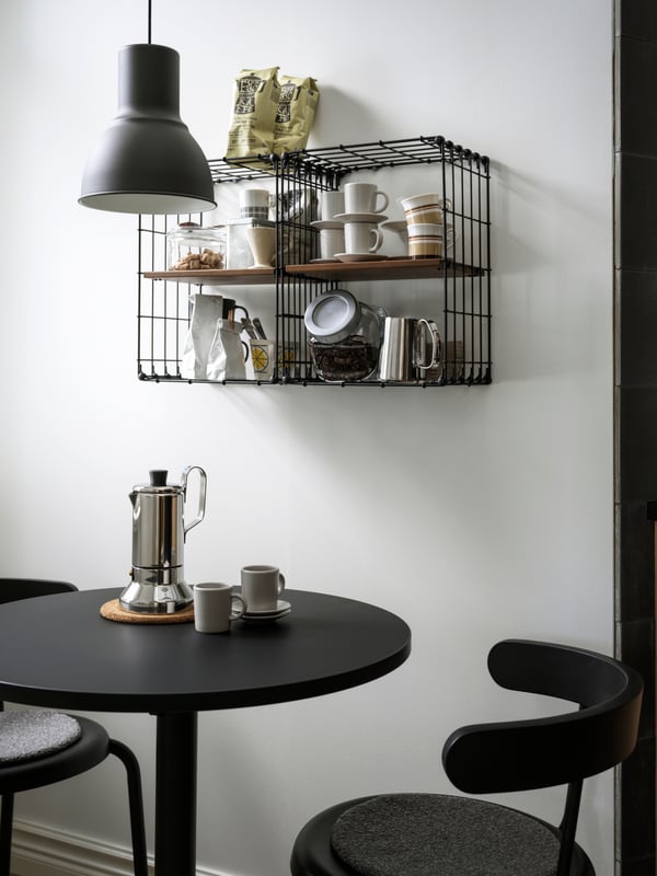 Deux étagères murales GULLHULT accueillant des accessoires pour le thé et le café, au-dessus d’une petite table ronde et de deux chaises.