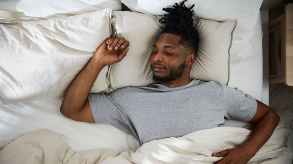 A man is sleeping comfortably in light coloured bedding