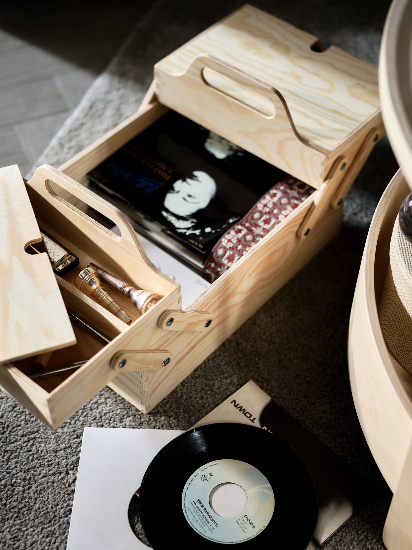 A natural-plywood KLÄMMEMACKA desk organiser stands on a rug with its sections parted, revealing musical accessories inside.