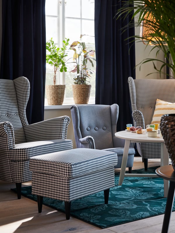 Two houndstooth-patterned STRANDMON wing chairs, and in between them stands a grey STRANDMON children’s armchair.