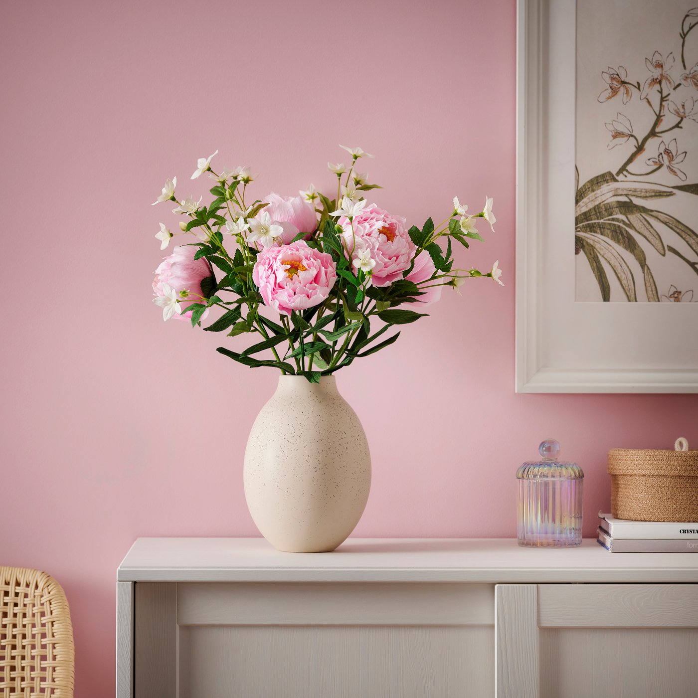 Vase mit rosa Blumen auf weißem Tisch vor rosa Wand.