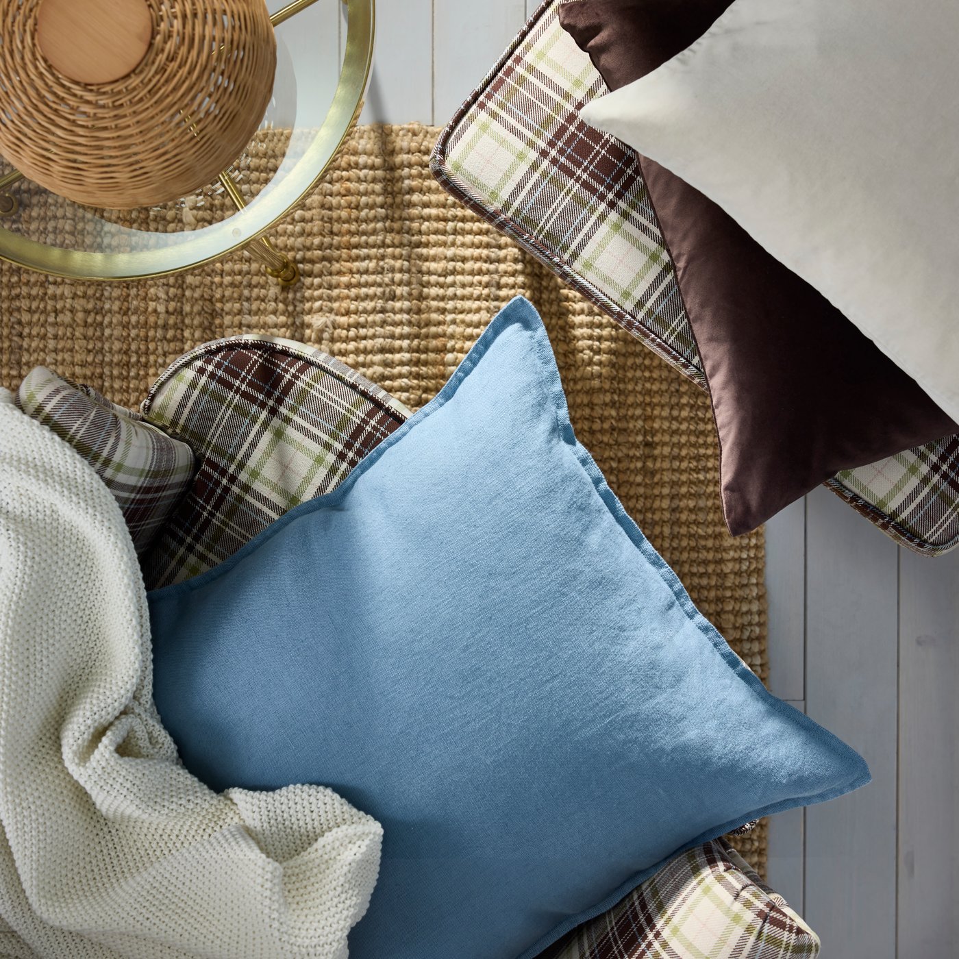 Coussin et jeté sur un fauteuil à oreilles et repose-pieds STRANDMON beige-brun au motif tartan baignés d’une douce lumière naturelle, près d’une table d’appoint TORSJÖ.