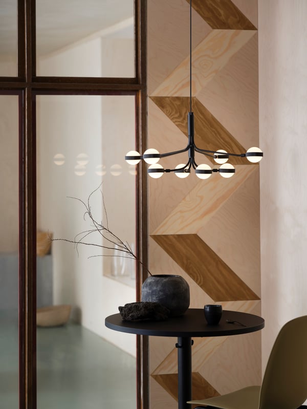 A STORSLINGA LED chandelier with eight arms in black and white is hanging over a small round STENSELE table in anthracite.