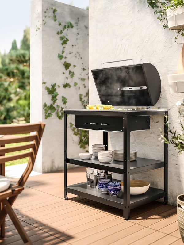 Una parrilla GRILLSKÄR con vegetales arriba apoyada en la pared de un patio.