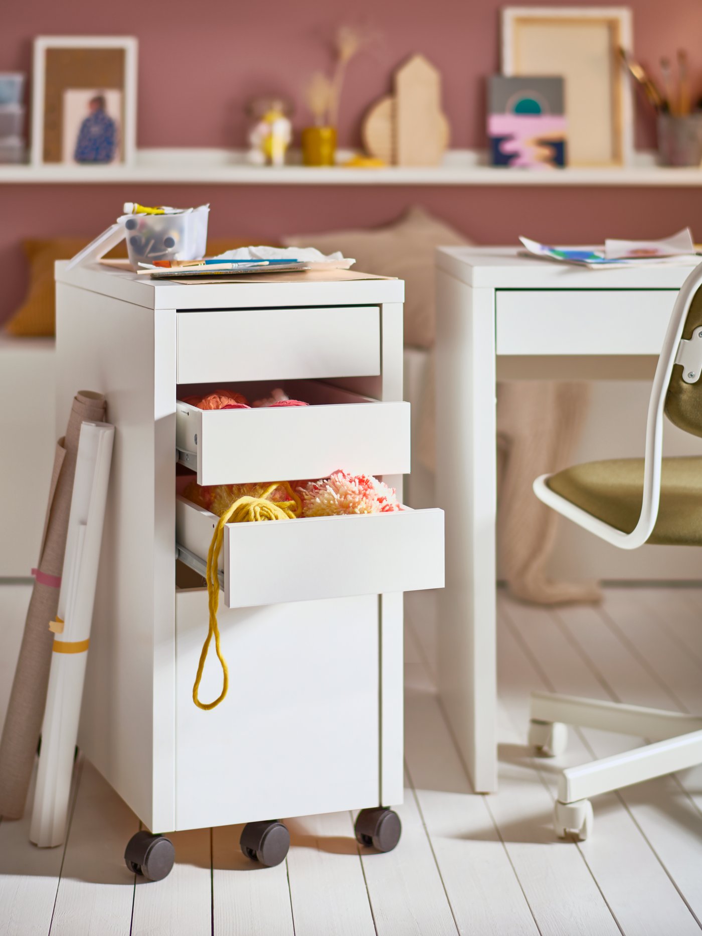 Un módulo de cajones blanco MICKE con espacio para carpetas colgantes y dos cajones llenos de lana, un escritorio infantil y una silla giratoria.