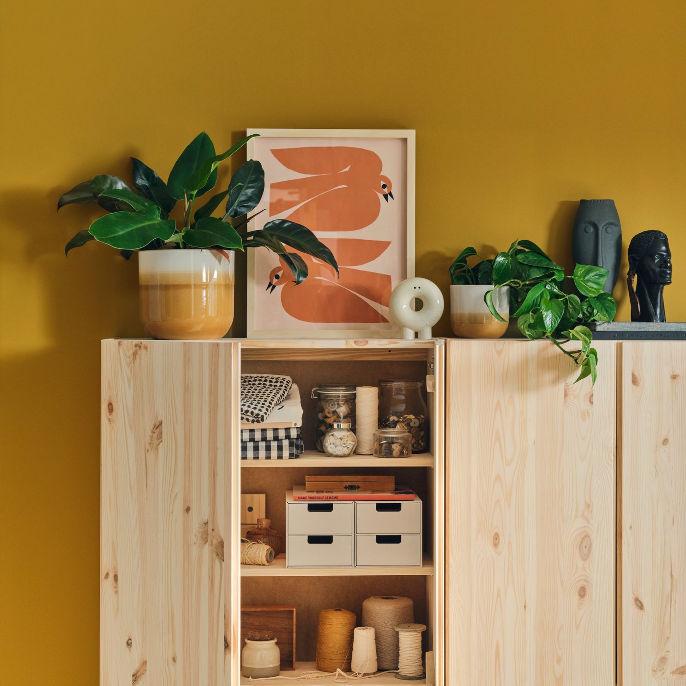 A pine IVAR base cabinet in a workspace, filled with craft supplies like yarn and buttons, against a yellow wall.