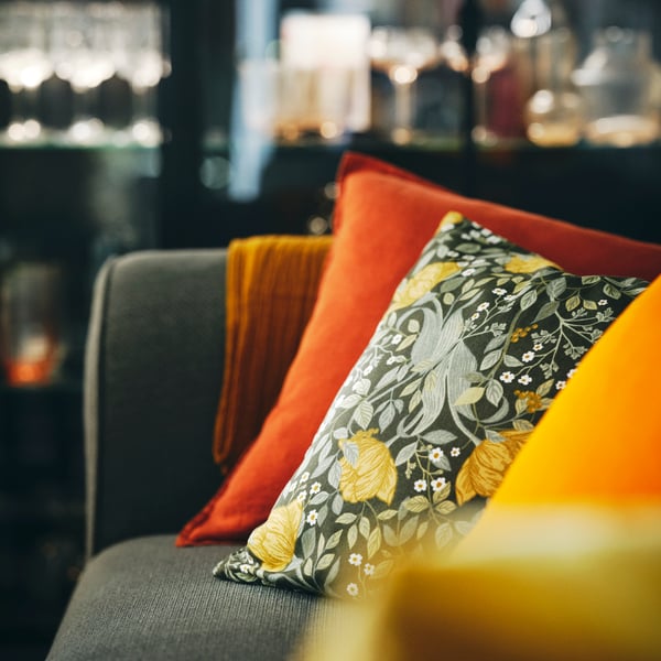 A sofa with a cushion in a red brown DYTÅG cushion cover and cushion in a deep green/floral pattern TUVSÄV cushion cover.