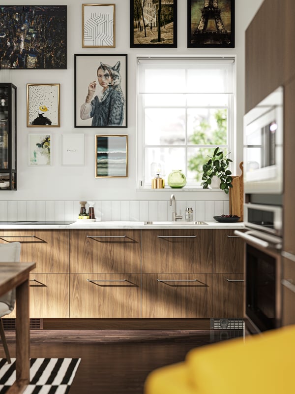 Una cocina con frentes TISTORP con efecto nogal café, piso de madera oscura y varios pósters en la pared junto a una ventana.