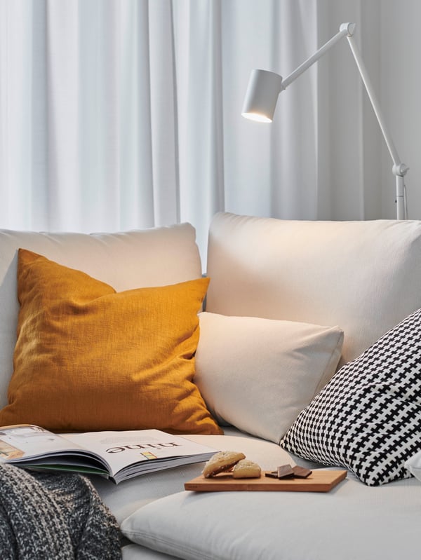 Dans un salon confortable, un homme est assis sur un canapé et lit un livre. Un lampadaire fournit une bonne lumière pour lire.