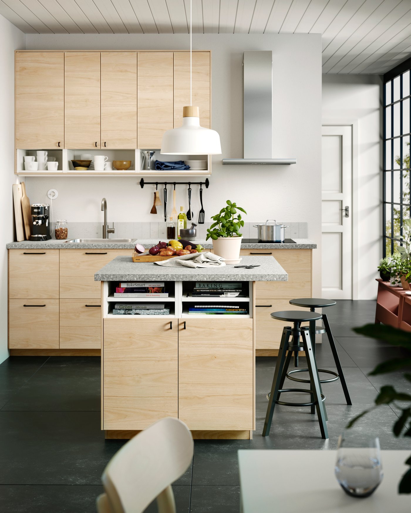 Světlá kuchyň IKEA s dřevěnými dvířky, ostrůvkem s úložným prostorem, šedou pracovní deskou, závěsným bílým svítidlem a černými barovými stoličkami.