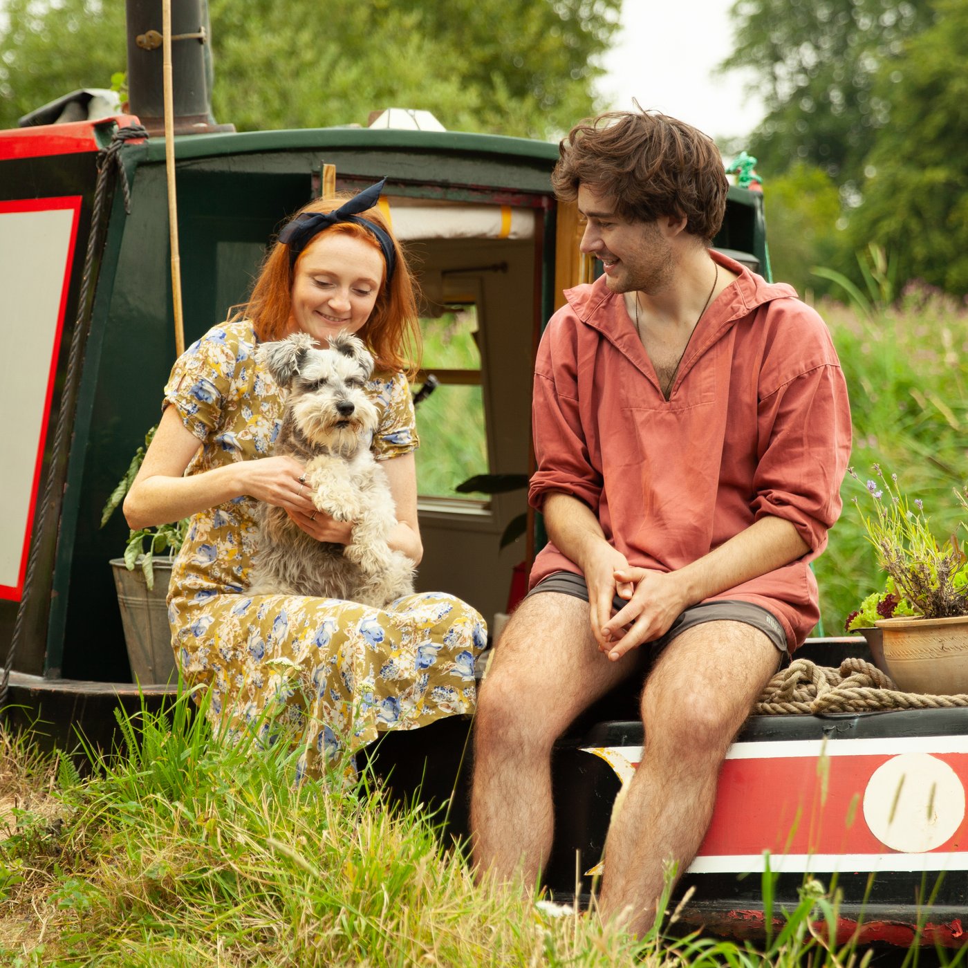 A woman, a man, and a small dog relax on the deck of a houseboat.