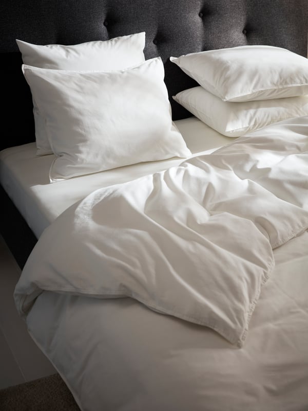 Una cama tapizada GLADSTAD en gris claro cubierta con ropa de cama NYPONLUGGMAL y una mesita de noche KNARREVIK en azul brillante junto a ella.

