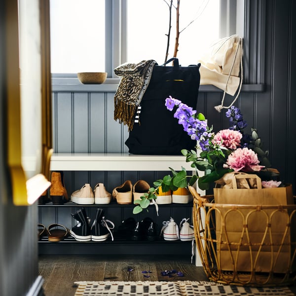Eine HEMNES Bank mit Schuhaufbewahrung und einem Korb mit frischen Blumen zur Rechten.