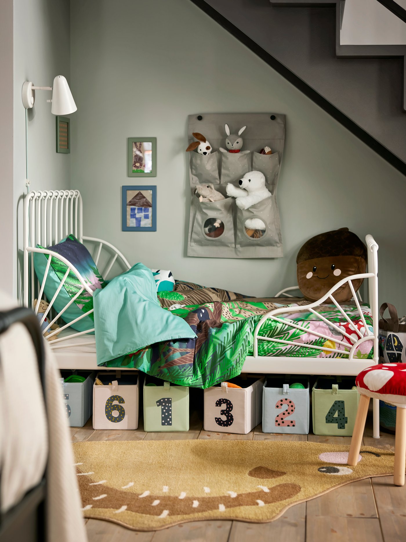 MINNEN extendable children’s bed in a corner of the room, with numbered storage boxes below and soft toys above.