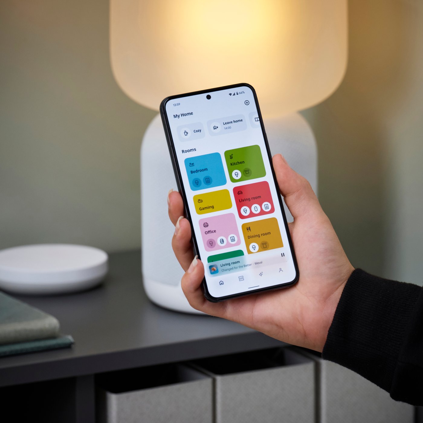 TRÅDFRI mrežni prolaz na stolu pored TRÅDFRI daljinskog upravljača i mobilni telefon na kom se vidi aplikacija IKEA Home smart.