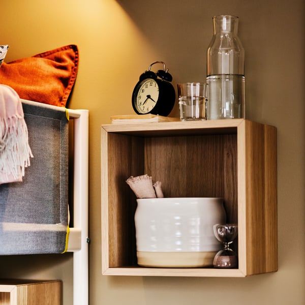 A DEKAD alarm clock atop an EKET cabinet that’s otherwise filled with tableware and wall-mounted next to a VITVAL loft bed.