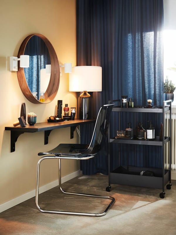 A black NISSAFORS cart and a blue/chrome chair by a brown-black wall shelf with a round mirror and white wall lamps.