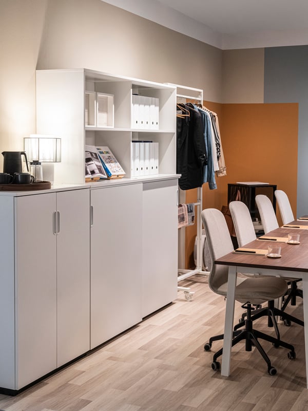 Une armoire GALANT blanche avec des portes est placée près d’une table et de chaises dans une salle de réunion.