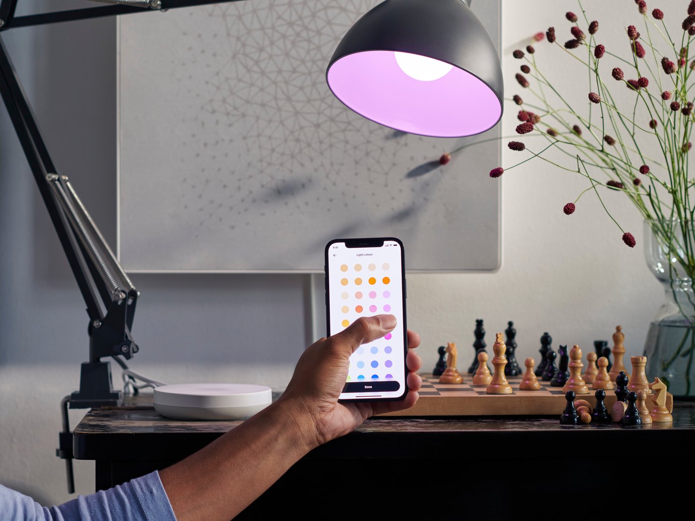 Iemand die de kleuren van een verbonden lamp aanpast met behulp van de IKEA Home-app.