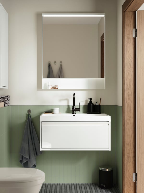 A bathroom featuring an ÄNGSJÖN wash-stand with drawer in high-gloss white, a BACKSJÖN wash-basin and a black mixer tap.