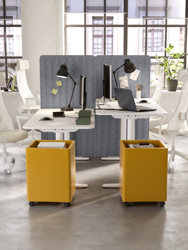 Two desks opposite each other, yellow storage cabinets on wheels, beige/white ergonomic chairs and black desk lamps.