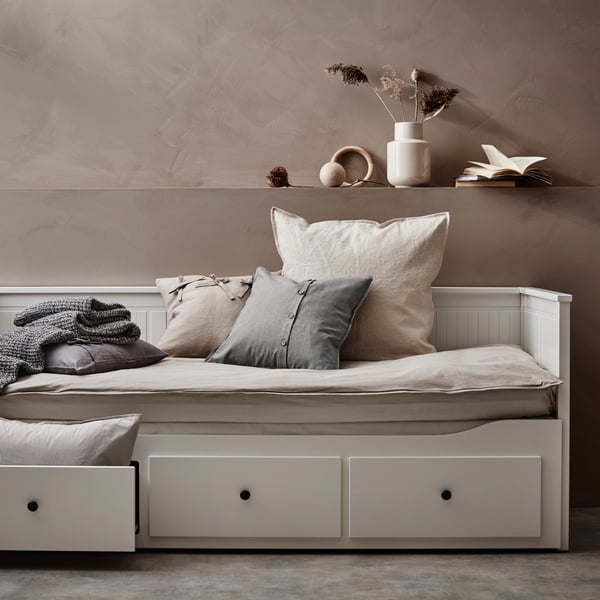 HEMNES dnevni krevet s 3 fioke/2 dušeka stoji uza zid. Na njemu su jastučići i jedna fioka je otvorena.