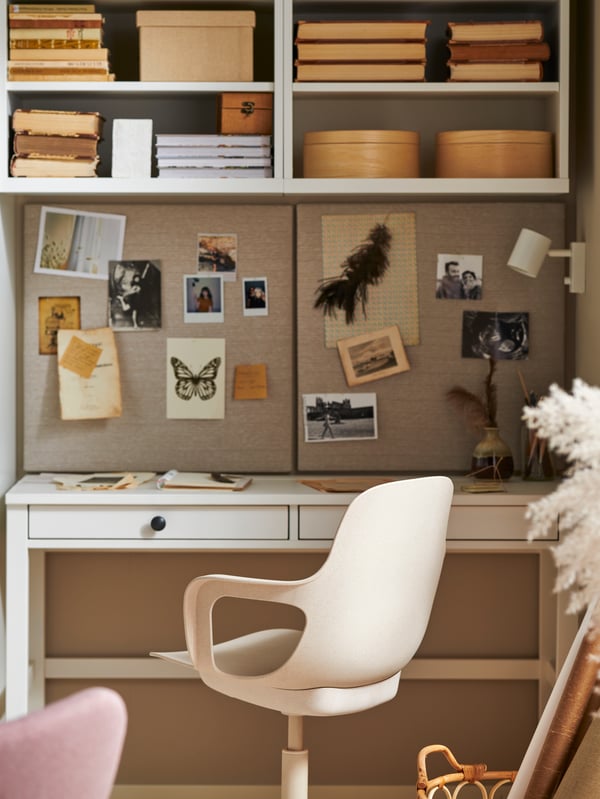 A workspace with a white stain HEMNES desk with two drawers, a swivel chair, shelves with books and boxes and two memo boards.