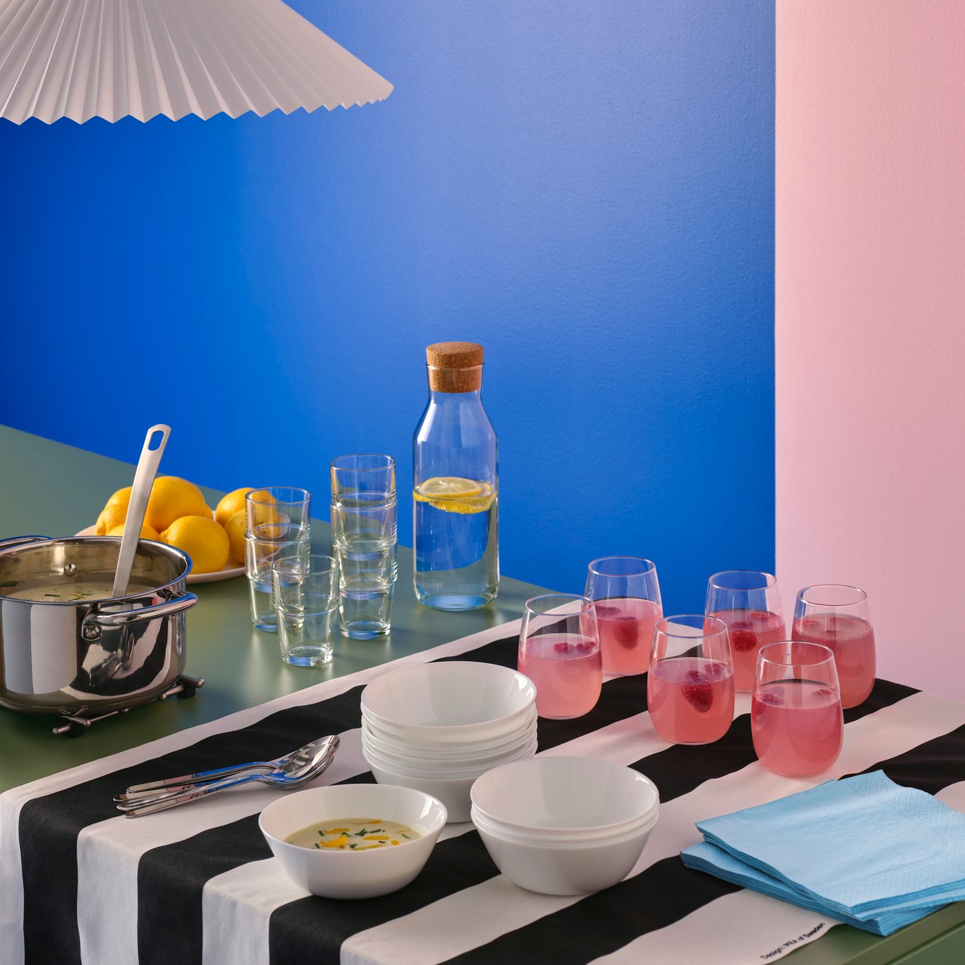 Raznobojni servant za supu s naslaganim OFTAST činijama, STORSINT čašama u kojima je roze piće i IKEA 365+ karafom s vodom.