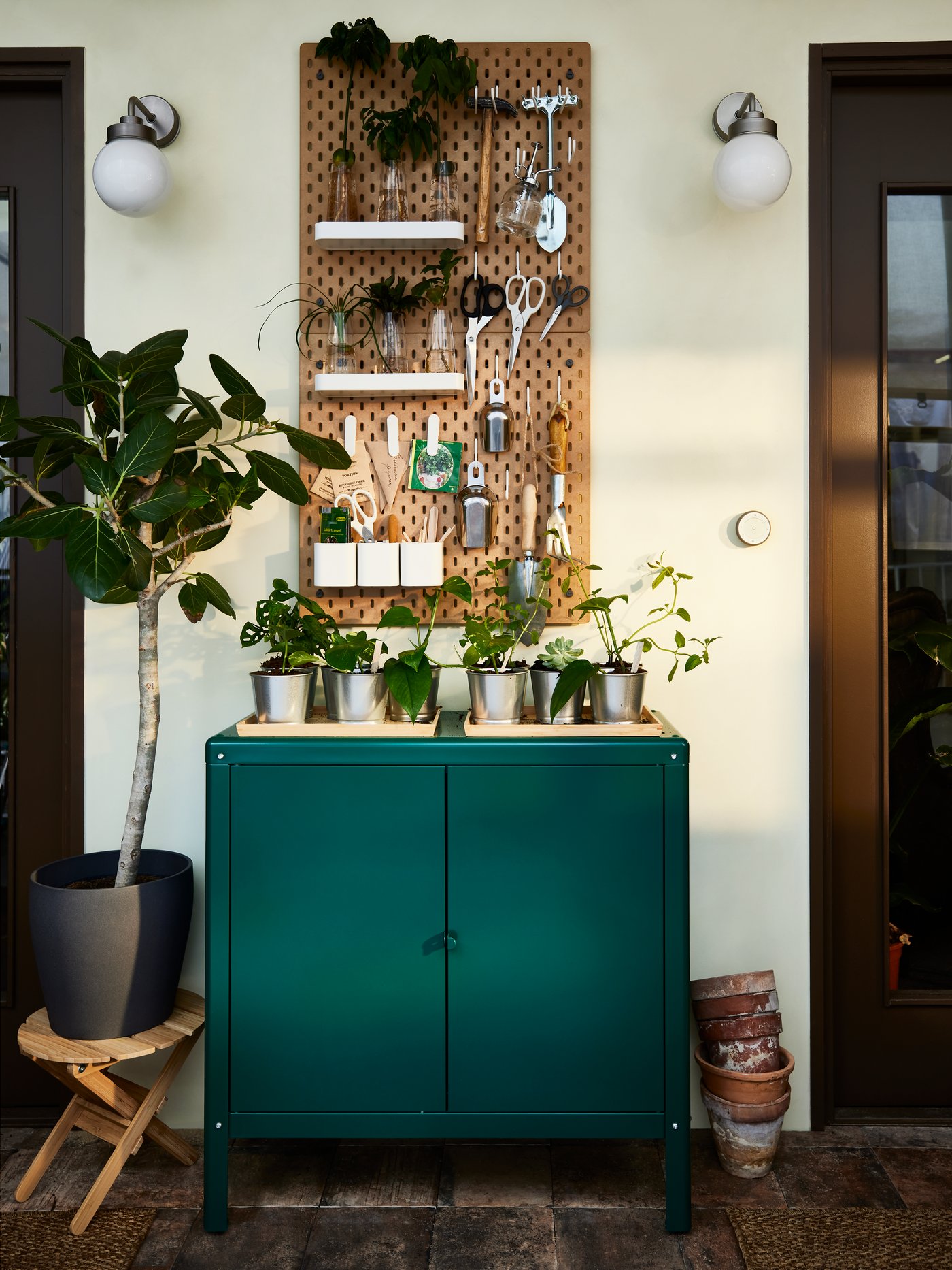 A green storage cabinet with various pots, plants and gardening tools on top.