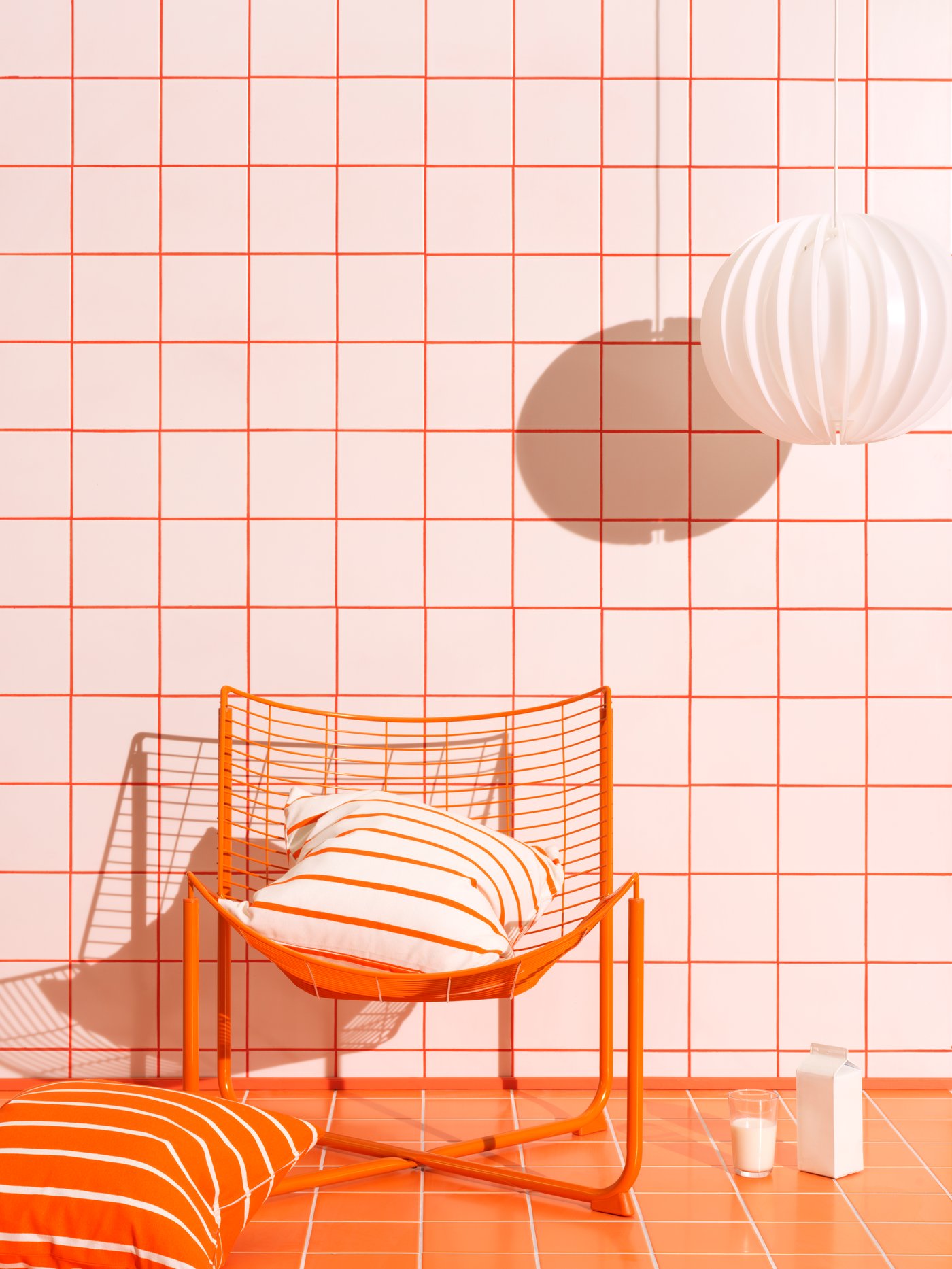 Ruimte in wit en oranje met een oranje kussen, een oranje stoel en een witte hanglamp.