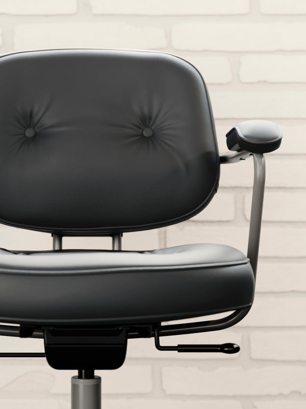 The thick, padded leather seat and back of a black ALEFJÄLL office chair, placed in front of a white brick wall.