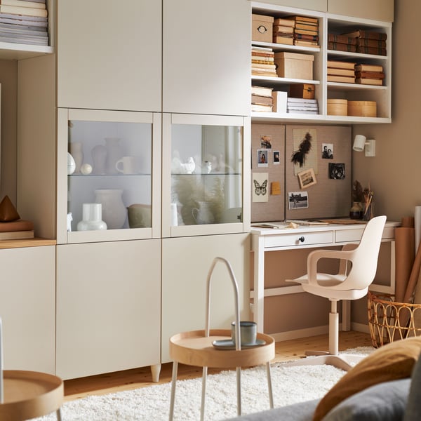 Warmly lit living room featuring the BESTÅ storage combination, white stain HEMNES desk with two drawers and a swivel chair.
