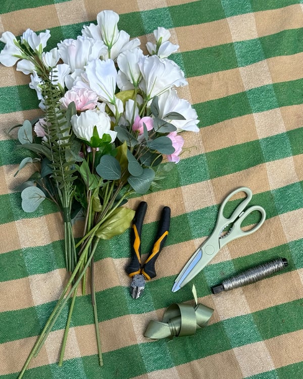 Konstgjorda midsommarblommor ligger på en filt bredvid en sax och sekatör.
