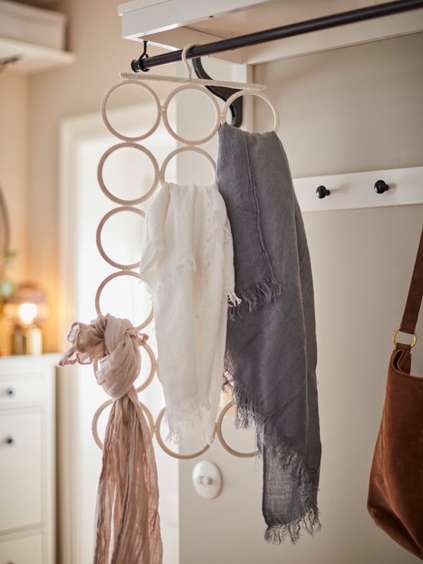 Hanging from a wardrobe rod is a KOMPLEMENT multi-use hanger holding necklaces, a scarf and other accessories.
