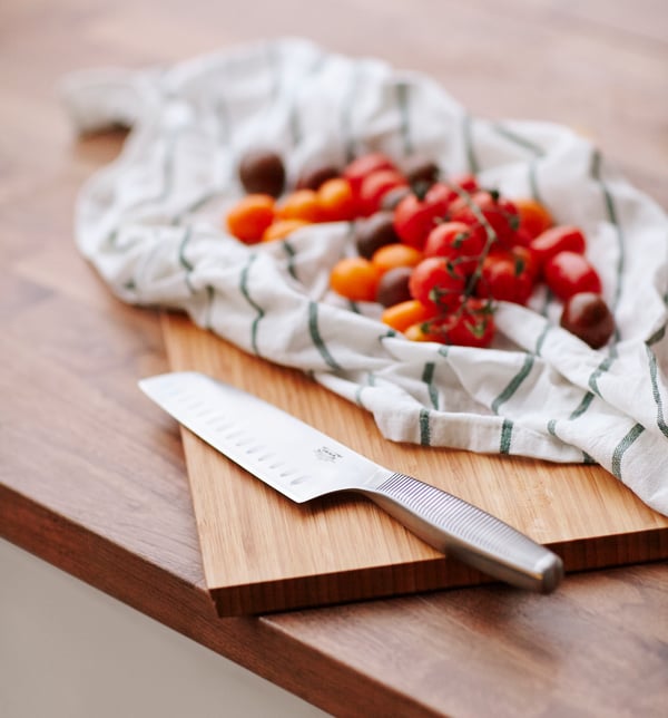 There is an IKEA 365+ vegetable knife in stainless steel on a wooden chopping board next to tomatoes on top of a tea towel.