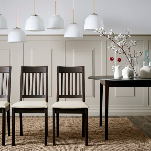 Four dark brown NÄSINGE chairs with light beige cushions are arranged around a black table in a stylish dining area.