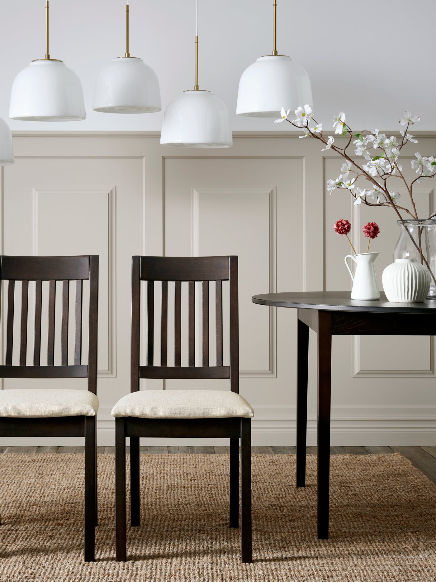 Four dark brown NÄSINGE chairs with light beige cushions are arranged around a black table in a stylish dining area.