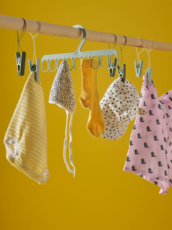 Colourful and patterned baby clothing hang from green SLIBB clothes pegs and SLIBB hanger in a bright yellow space.