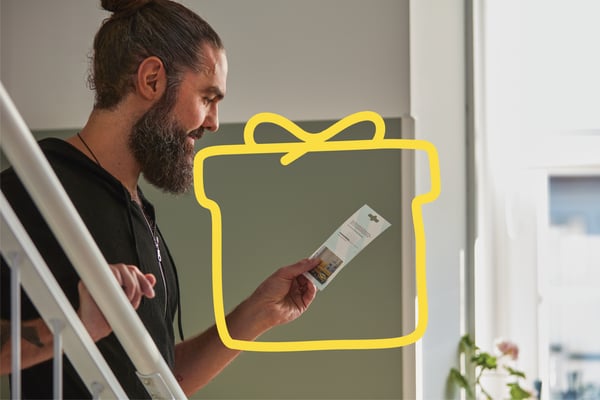 A man is looking at an IKEA voucher. There is a gift icon around it.